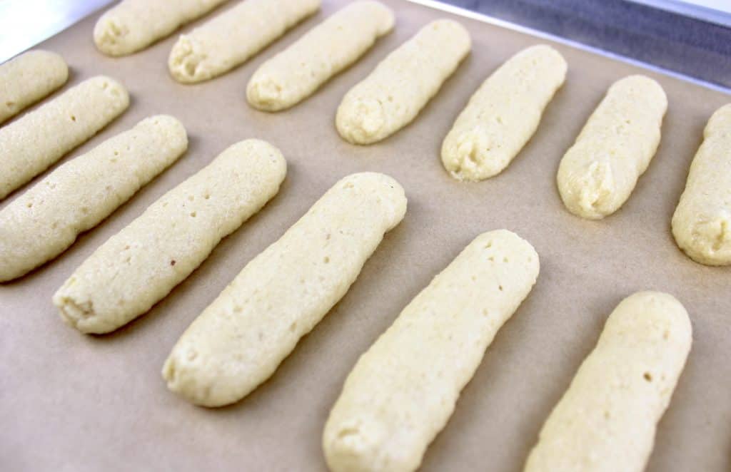 lady fingers batter piped onto baking sheet with parchment paper
