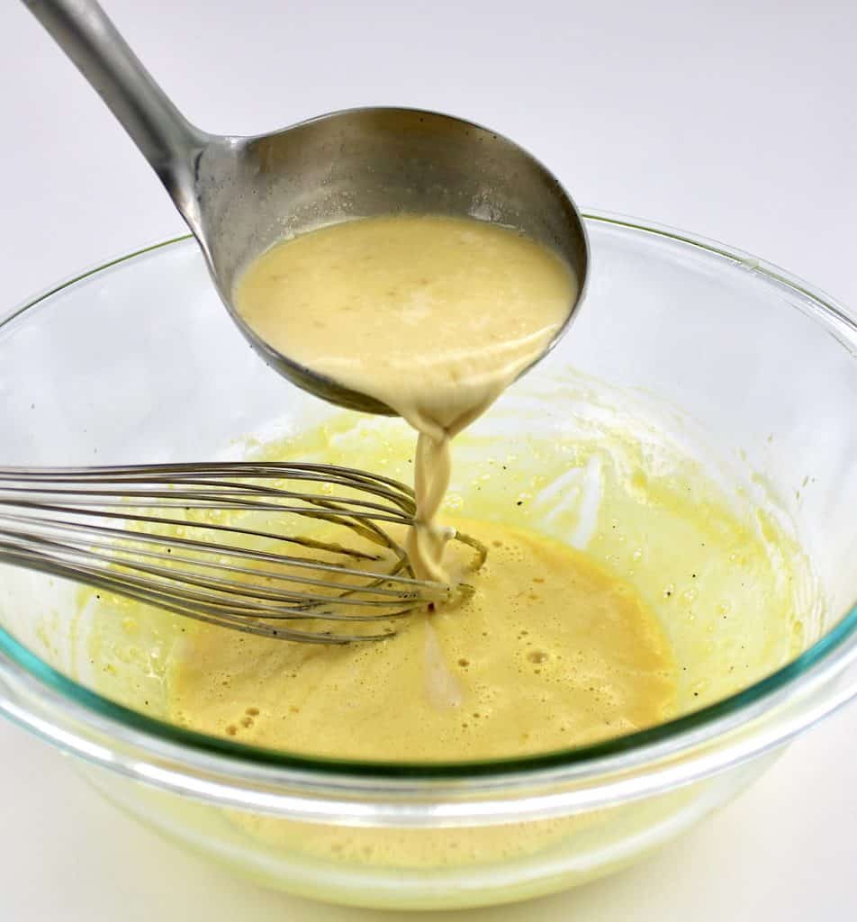 ladle dripping custard into egg yolks in glass bowl with whisk