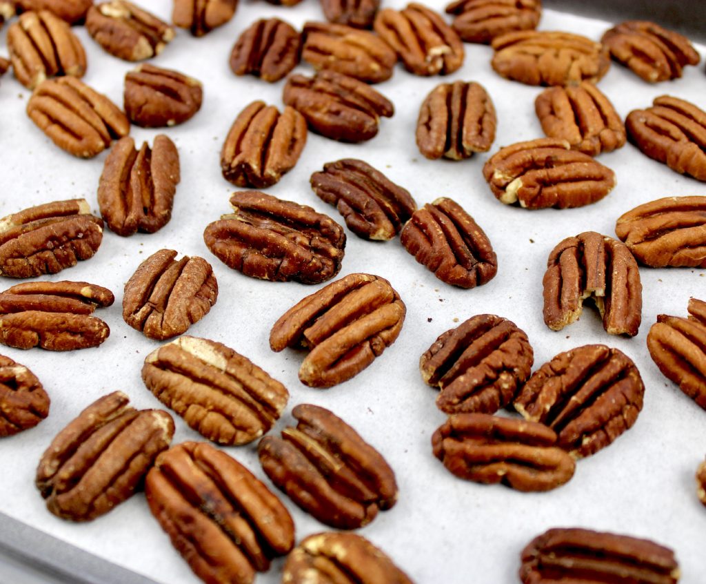 pecan halves toasted on baking sheet with white parchment paper