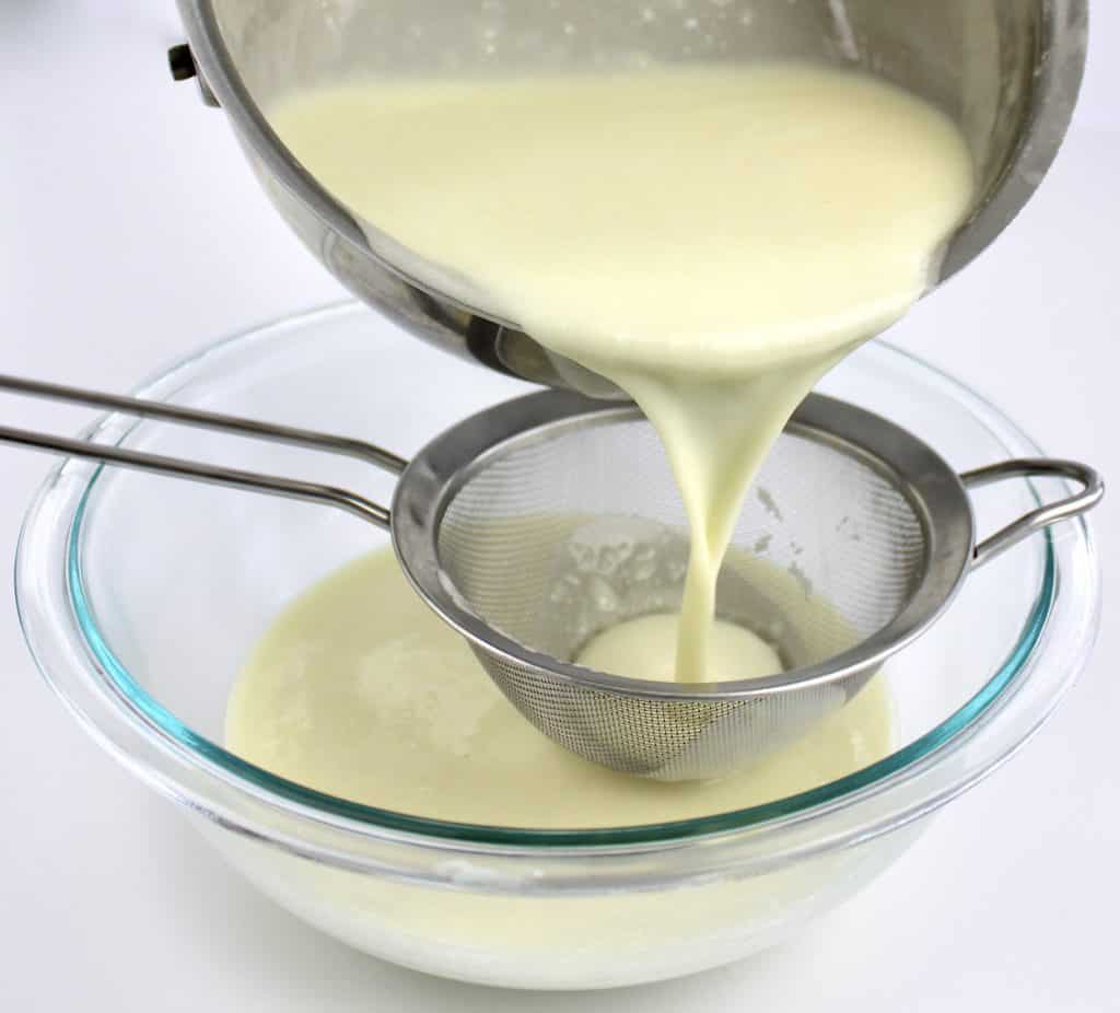 coconut ice cream custard being poured through sieve in glass bowl