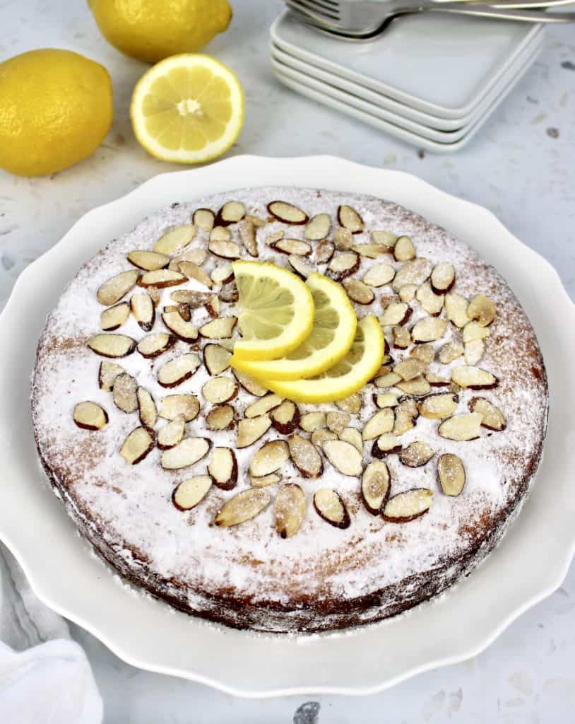 lemon ricotta cake with powdered sugar sliced almonds and 3 lemon slices on top