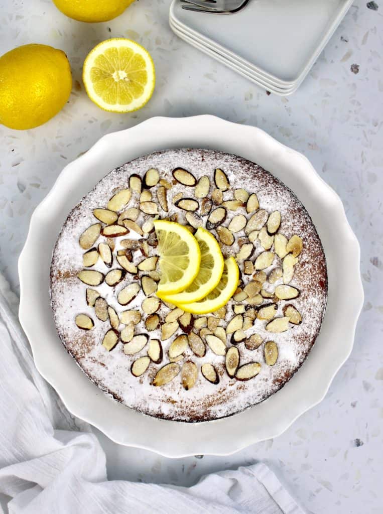 lemon ricotta cake with powdered sugar sliced almonds and 3 lemon slices on top