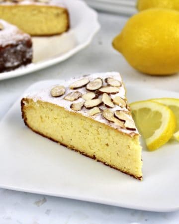 slice of lemon ricotta cake on white plate with cake in background