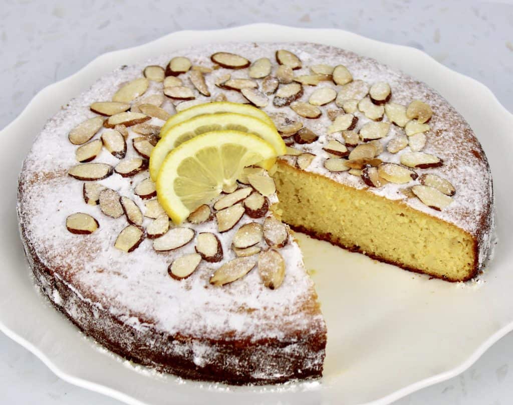 lemon ricotta cake with powdered sugar sliced almonds and lemon slices with slice missing