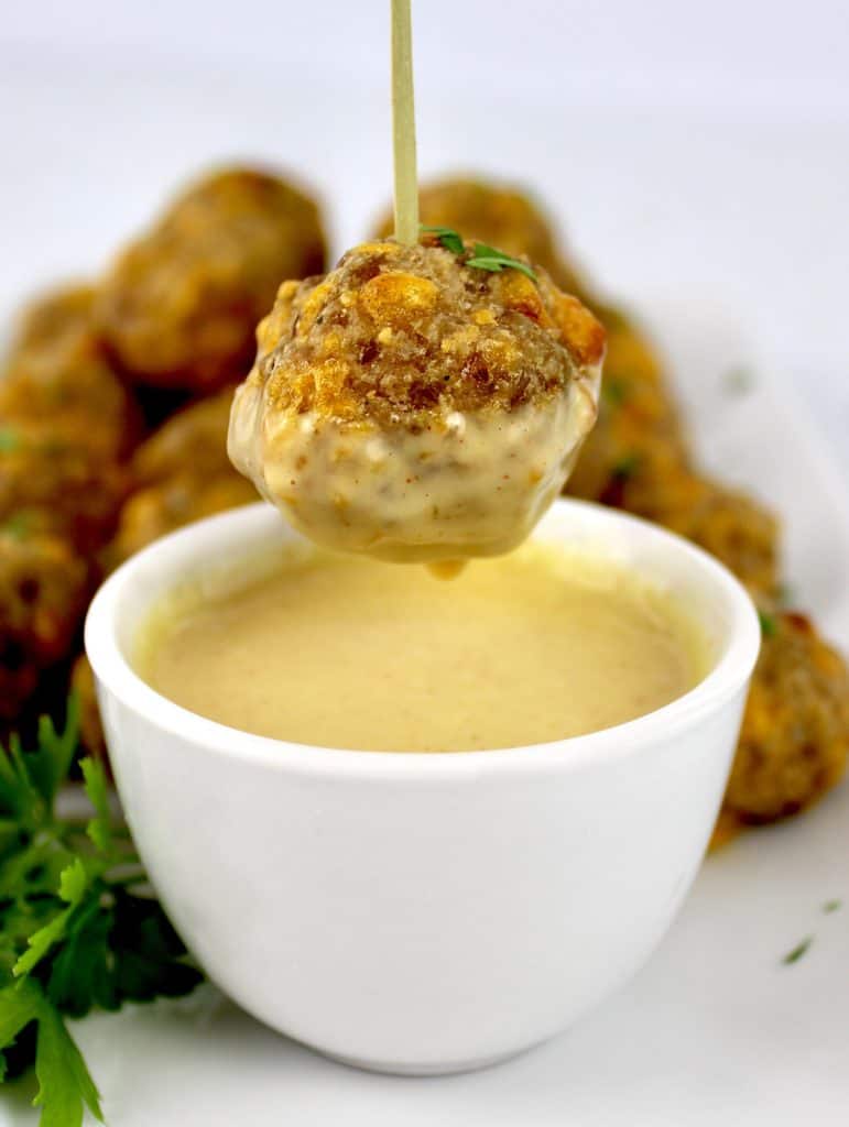 sausage ball on skewer being dipped into honey mustard sauce in white bowl