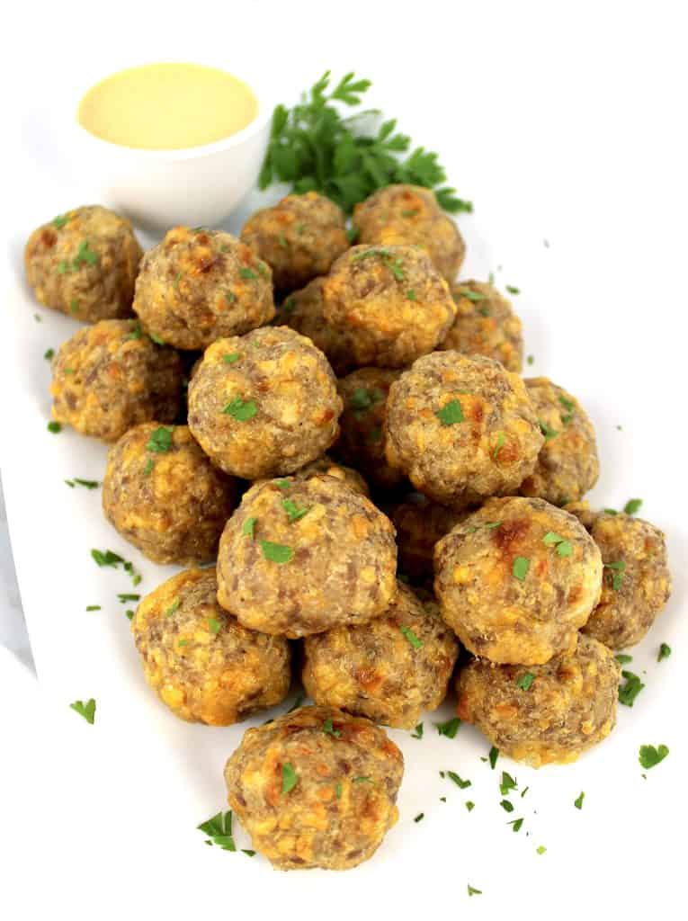 sausage balls piled up on white plate with dipping sauce and parsley on side
