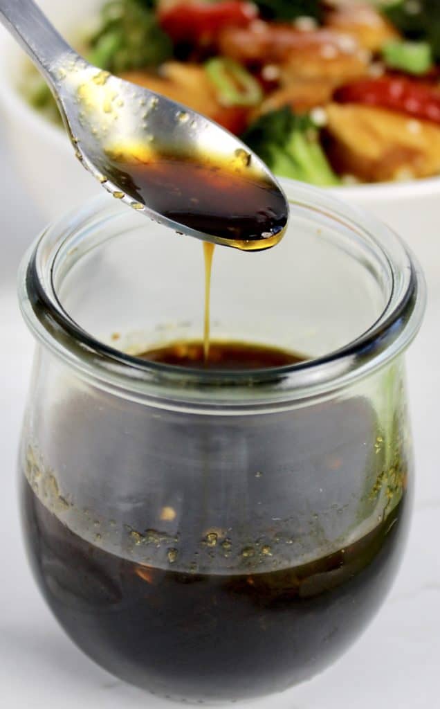 Keto Teriyaki Sauce being spooned out of glass jar with stir fry bowl in background