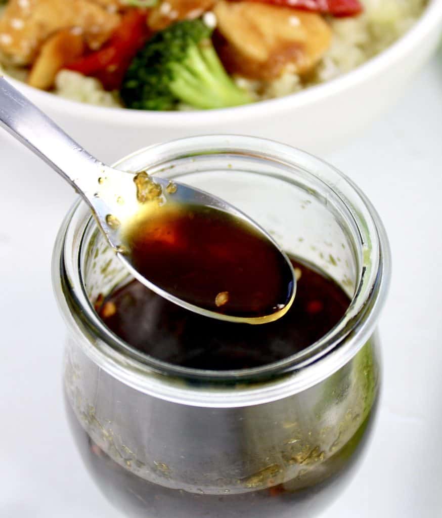 Keto Teriyaki Sauce being spooned from open jar with stir fry bowl in background