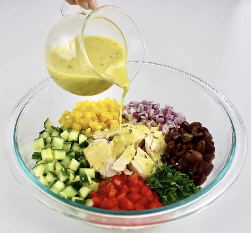 lemon dressing being poured over diced veggies and tuna in glass bowl