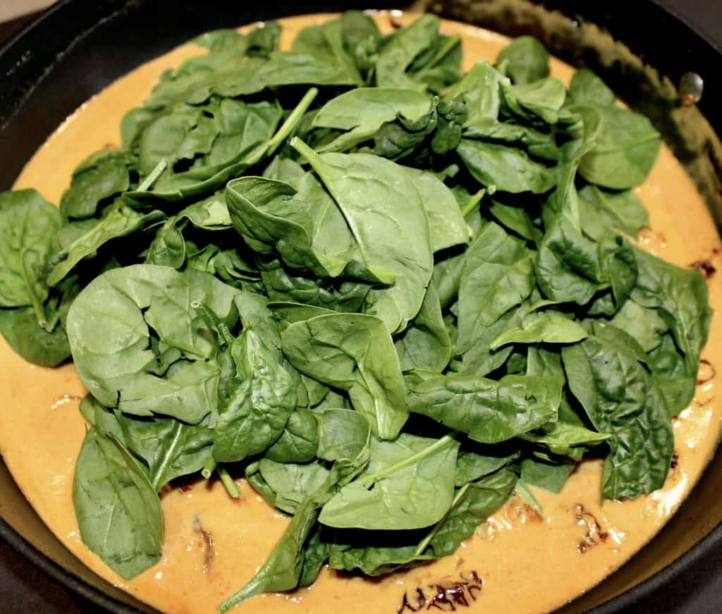 tuscan sauce in skillet with raw spinach leaves on top