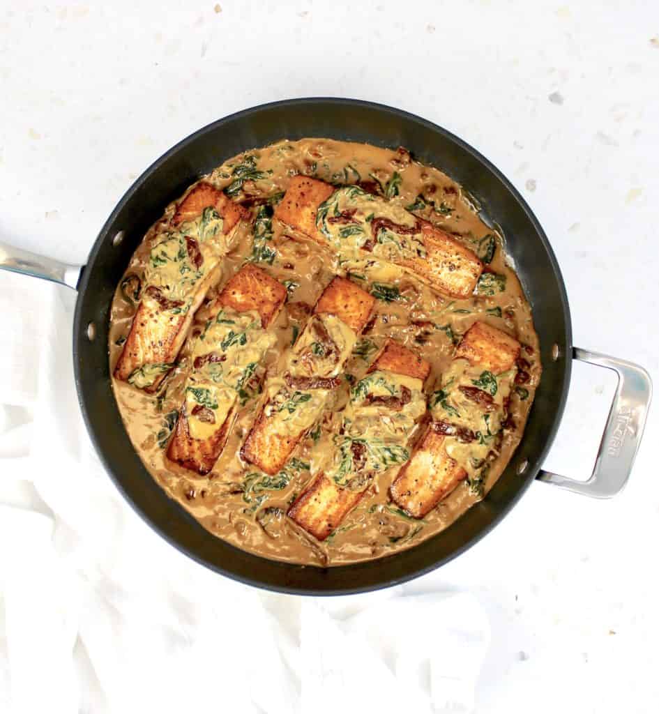 overhead view of 6 pieces of salmon in cream sauce in skillet