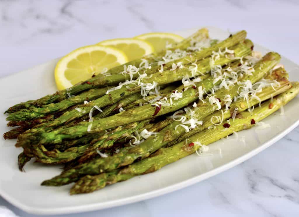 closeup of roasted asparagus with grated cheese and lemon slices