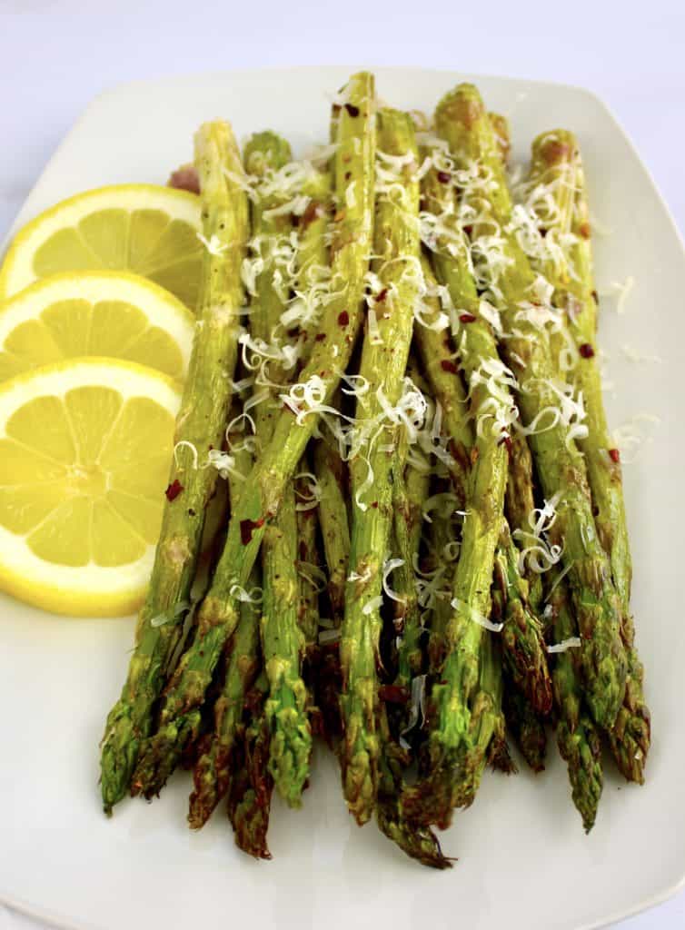 roasted asparagus on white plate with grated parmesan 3 lemon slices