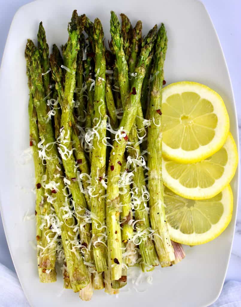 roasted asparagus on white plate with grated parmesan 3 lemon slices