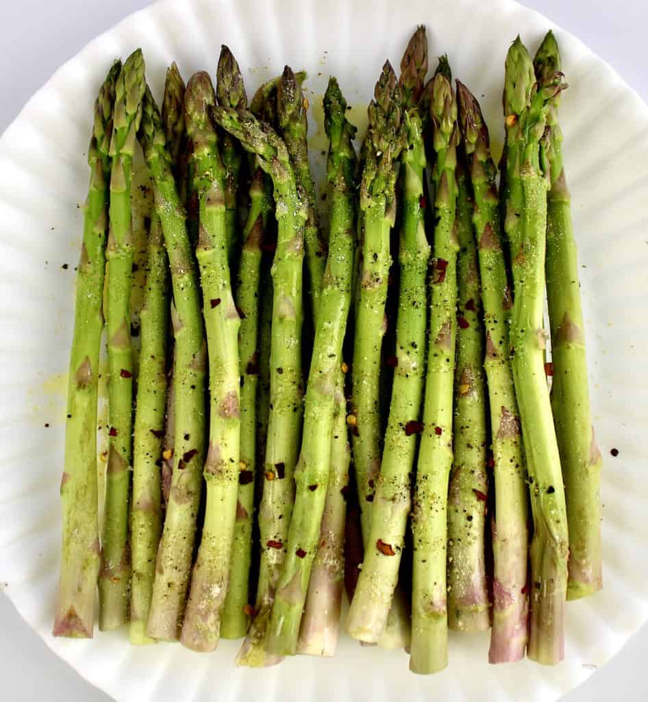 raw asparagus on white plate with olive oil and spices on top