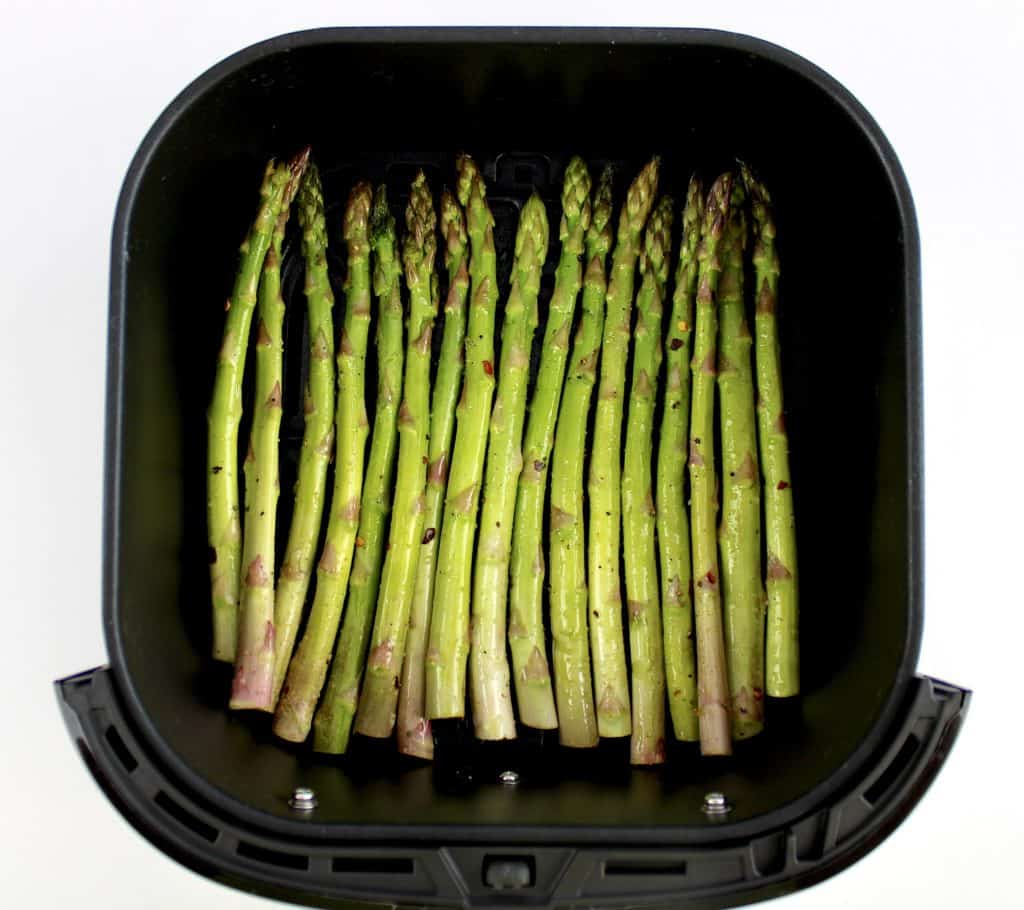 raw asparagus with olive oil and spices in air fryer basket