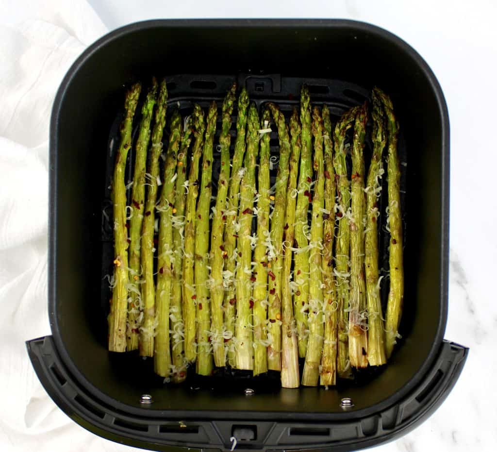 roasted asparagus in air fryer basket with grated parmesan on top