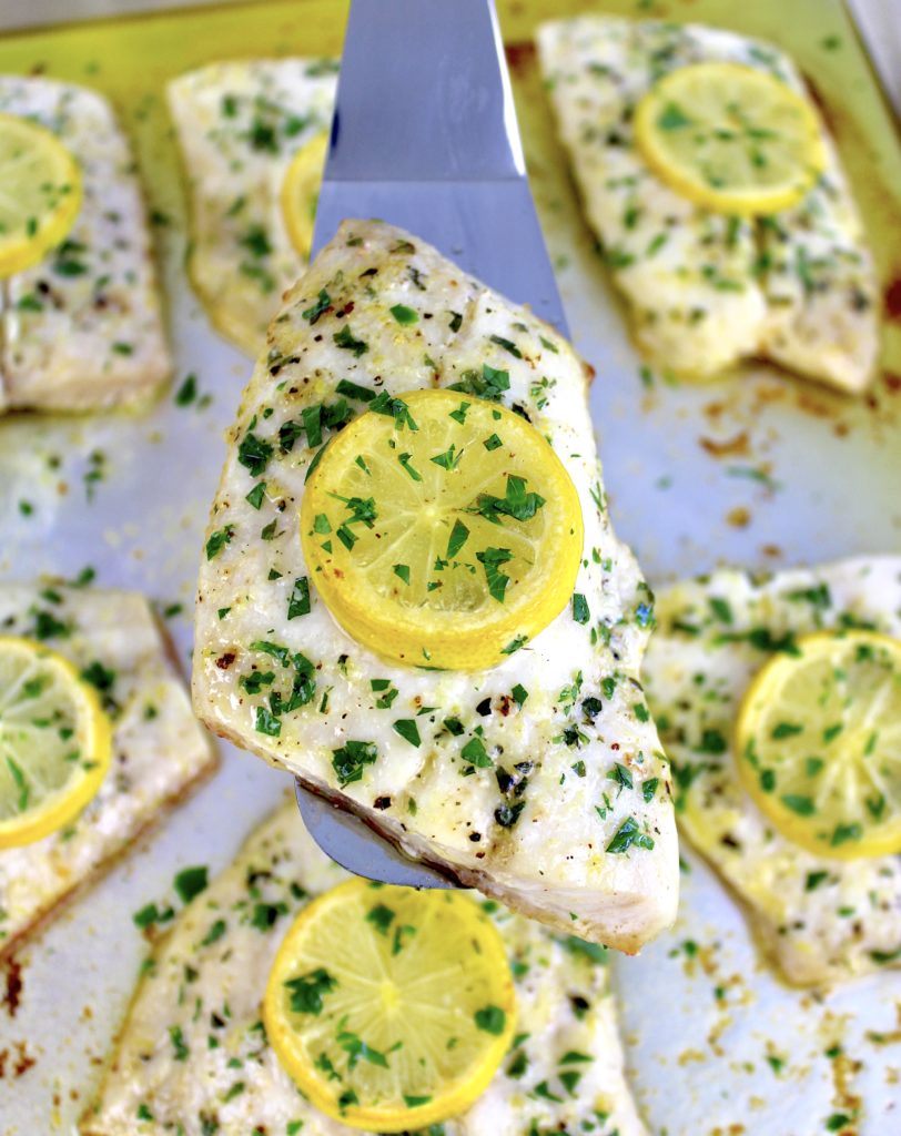 piece of baked red snapper with herbs and lemon slice on top being held up with silver spatula