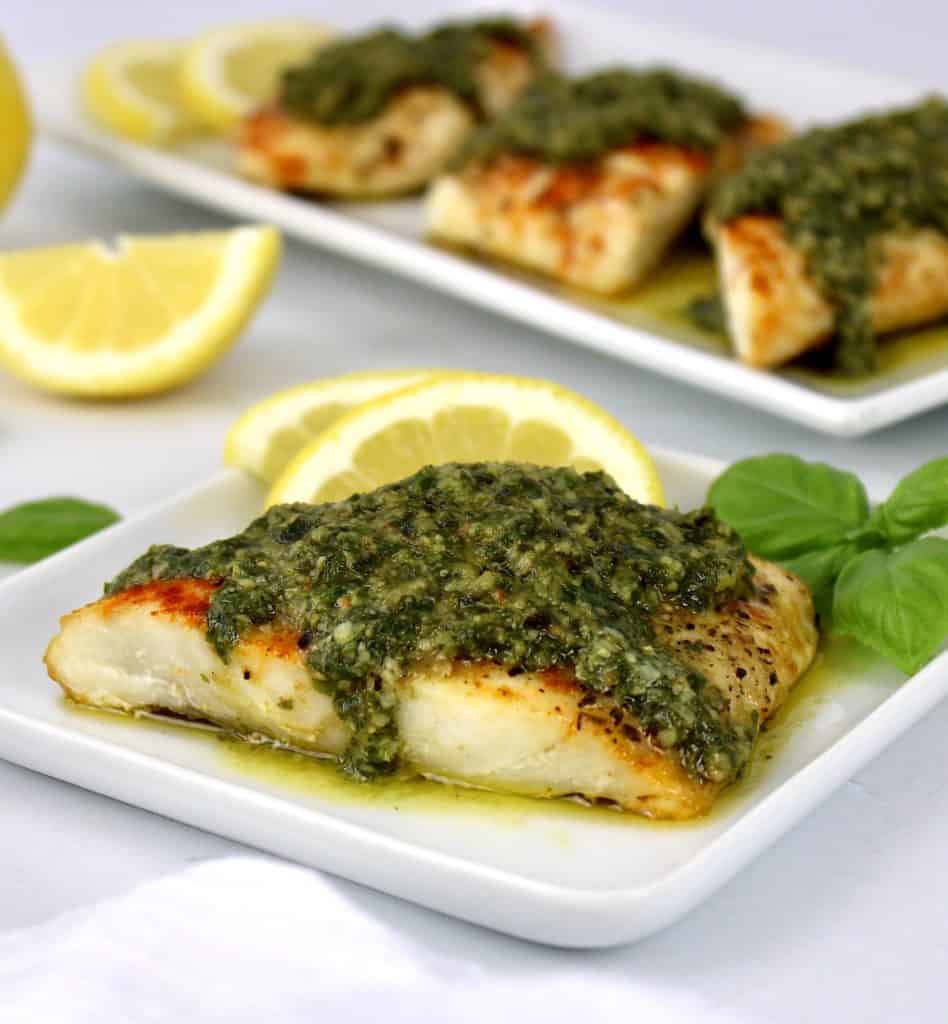 overhead view of 4 pieces of snapper with pesto on top and lemon slices on side