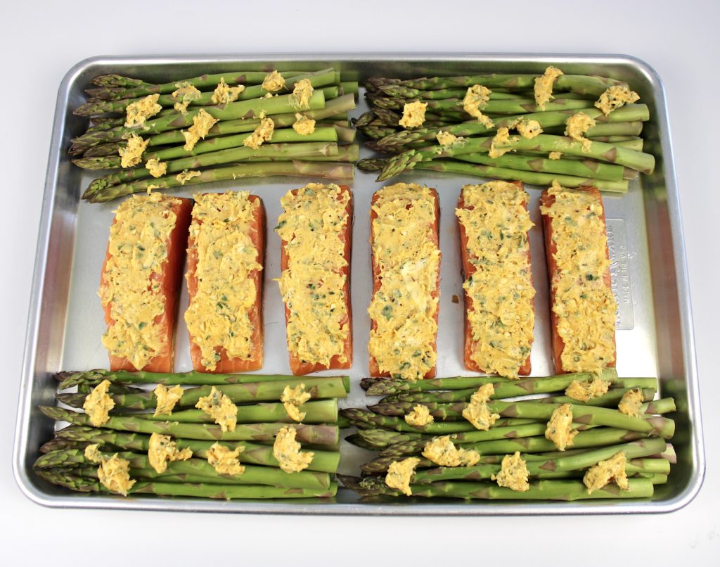 6 pieces of salmon and 4 bunches of asparagus on sheet pan with compound butter spread all over