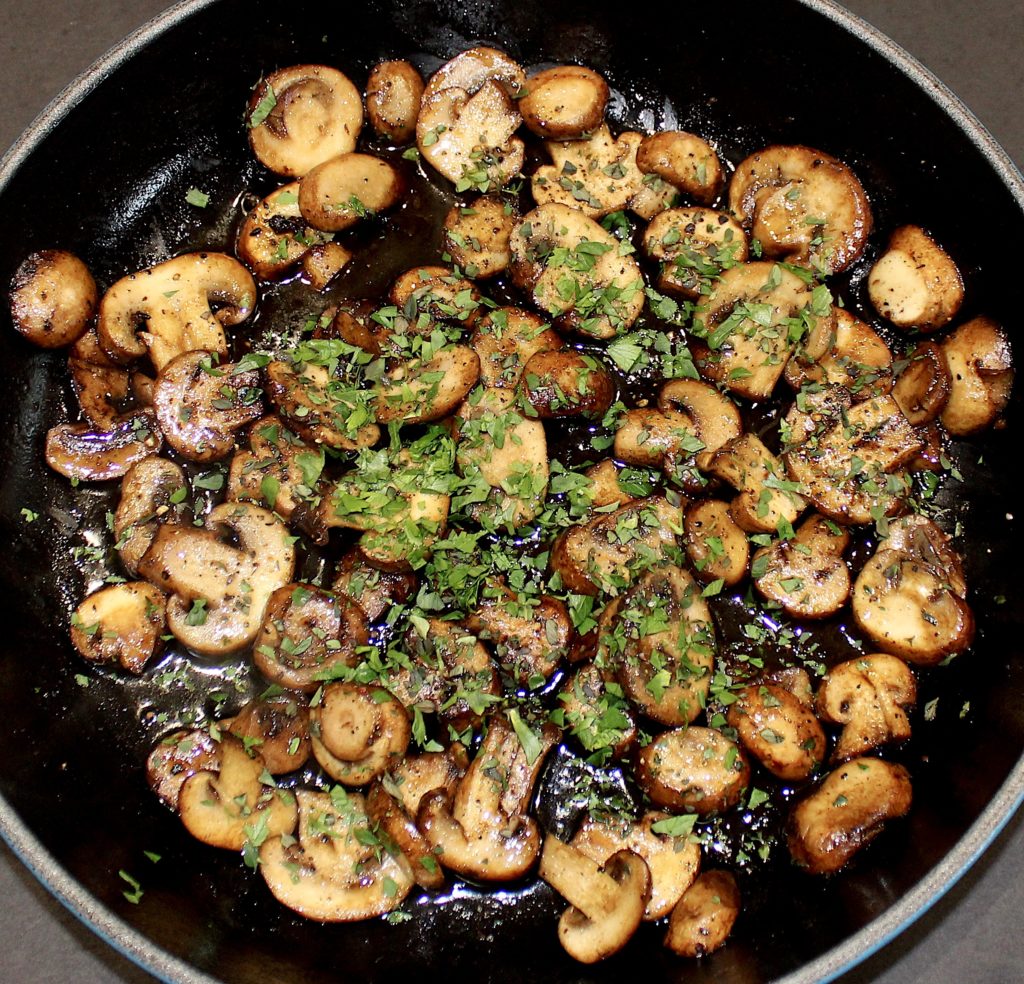Sauteed mushrooms in skillet with chopped parsley on top