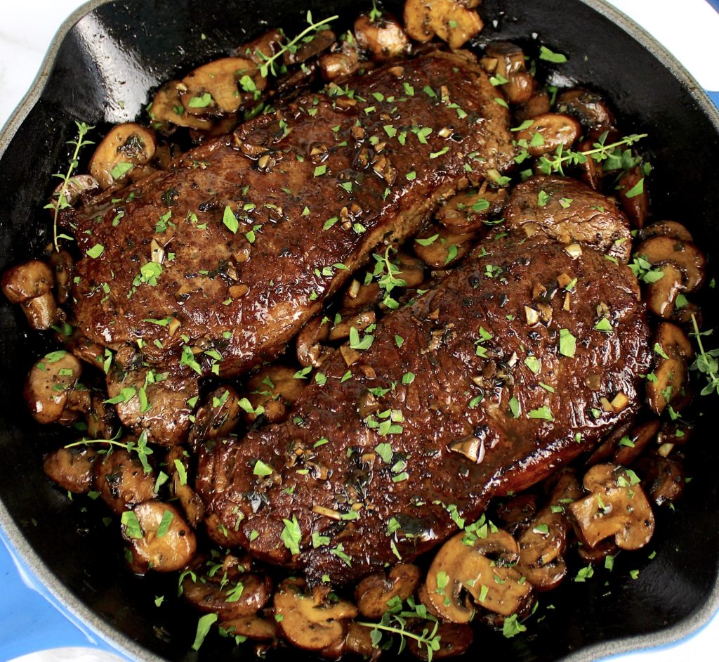 2 steaks in skillet cooked with mushrooms and parsley on top