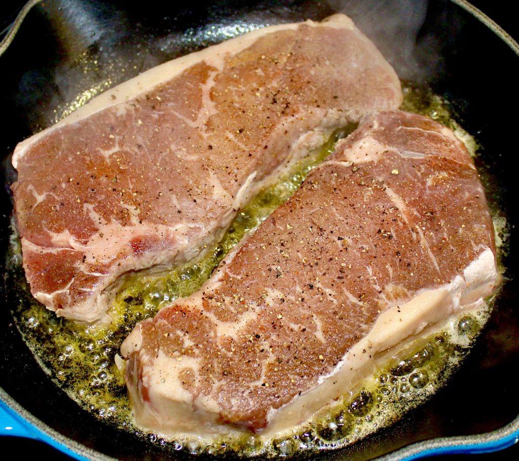 2 raw steaks with salt and pepper frying in skillet