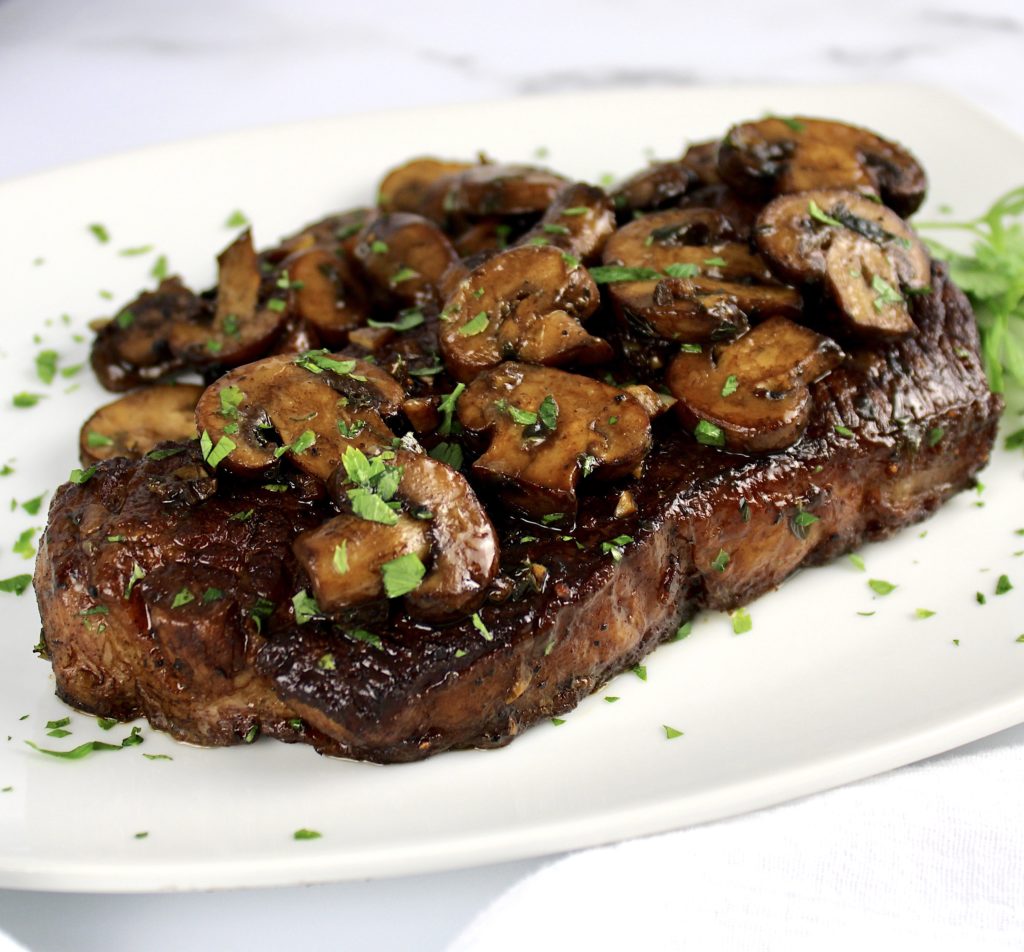 closeup of steak on white plate with sautéed mushrooms on top