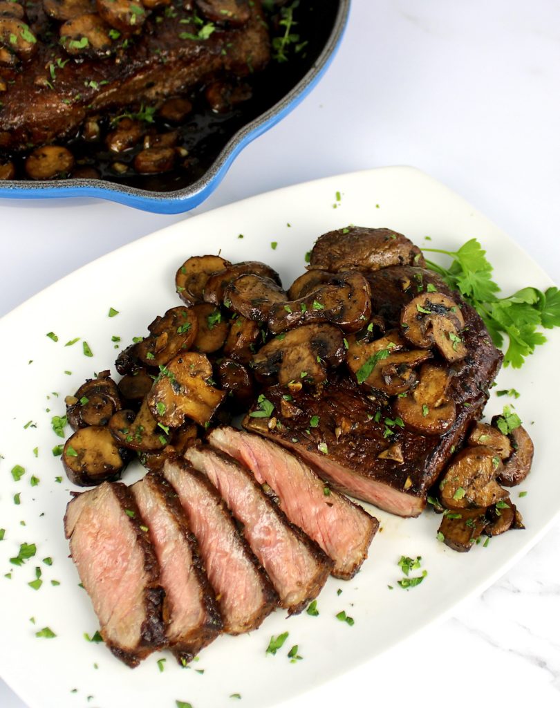 steak partially sliced on white plate with sautéed mushrooms on top