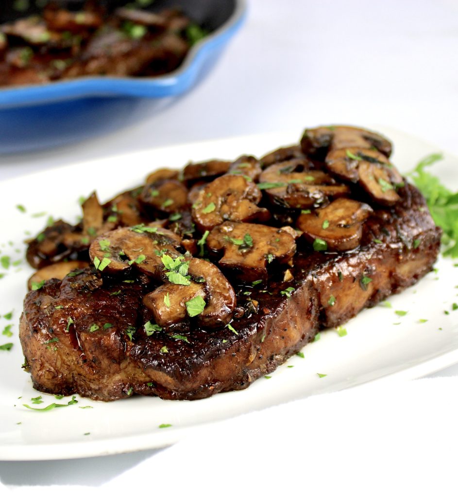 closeup of steak on white plate with sautéed mushrooms on top
