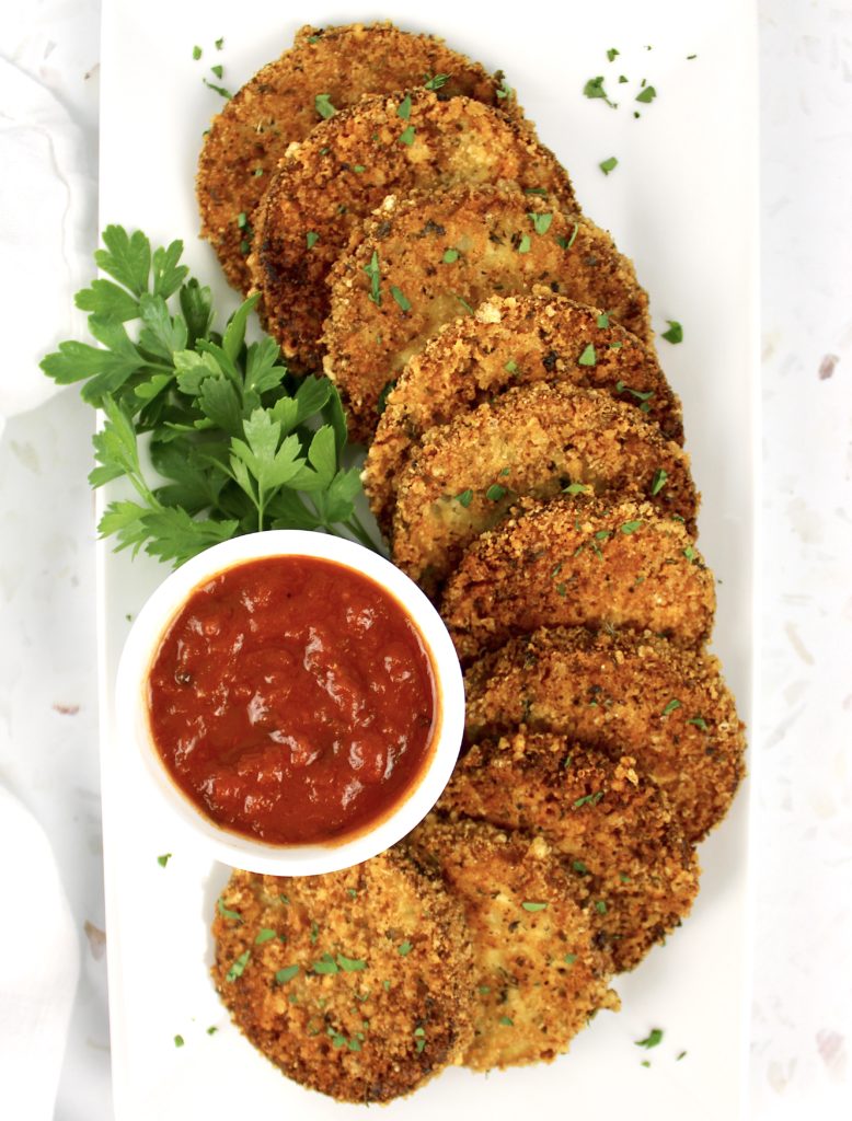 overhead view of fried eggplant rounds on white platter with marinara sauce in white cup