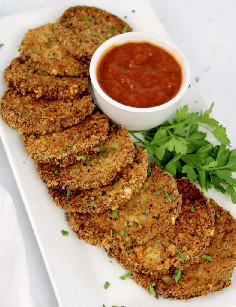 overhead view of fried eggplant rounds on white platter with marinara sauce in white cup