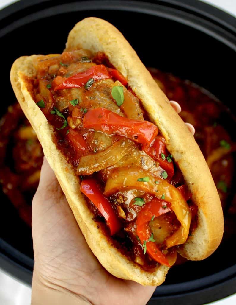 sausage and peppers in bun being held up by hand