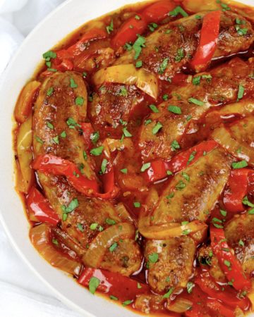 sausage with red and yellow peppers in marinara sauce in white bowl