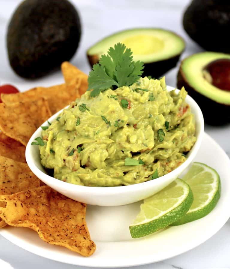 guacamole in white bowl with lime slices and tortilla chips on side