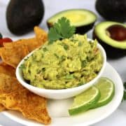 guacamole in white bowl with lime slices and tortilla chips on side