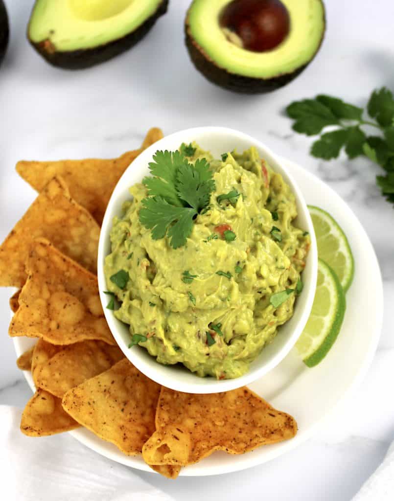overhead view of guacamole in white bowl with tortilla chips and lime slice on side