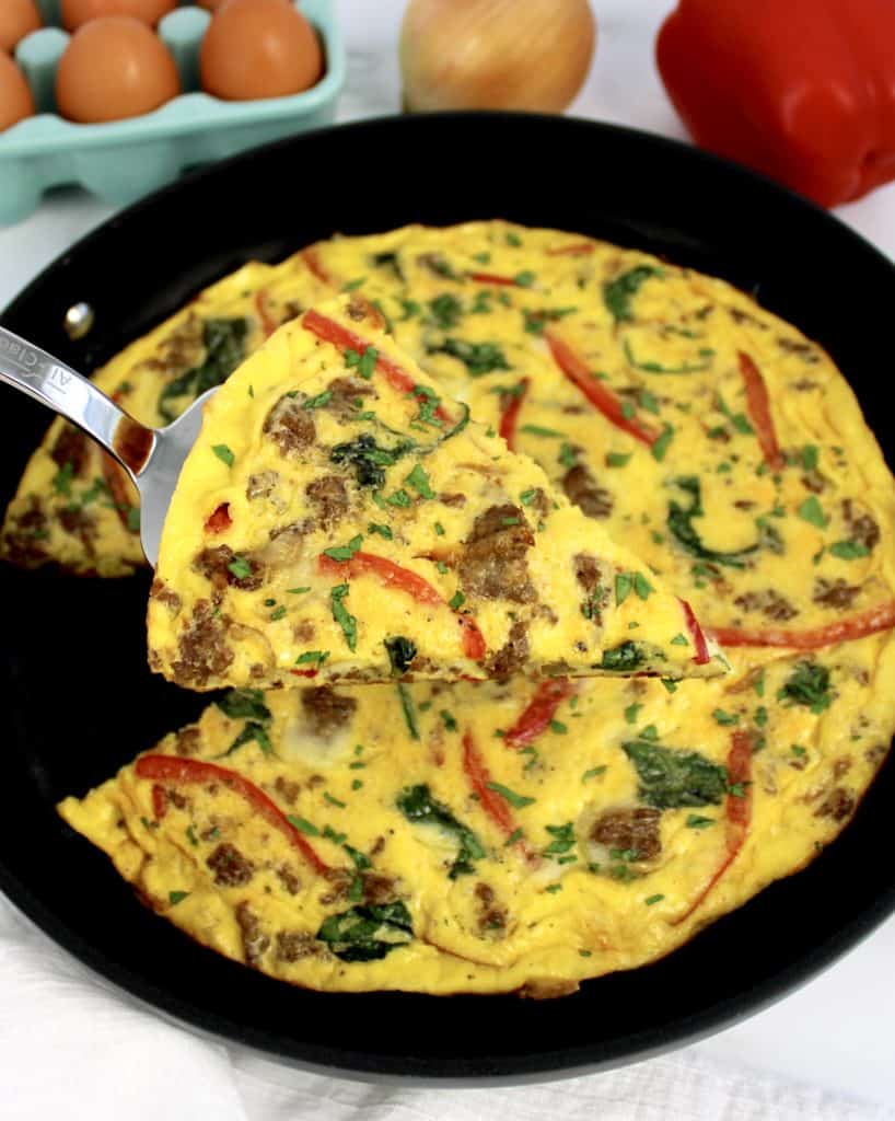 slice of sausage and pepper frittata being held up over skillet