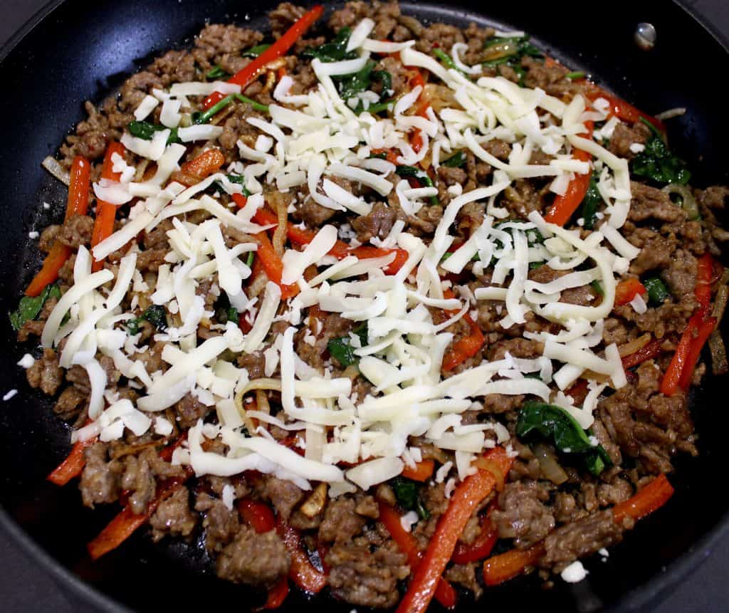 Italian sausage and peppers in skillet with shredded mozzarella on top