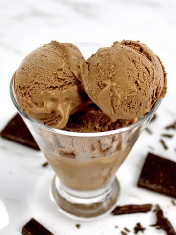 chocolate ice cream scoops in glass with chunks of chocolate on counter