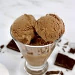 chocolate ice cream scoops in glass with chunks of chocolate on counter