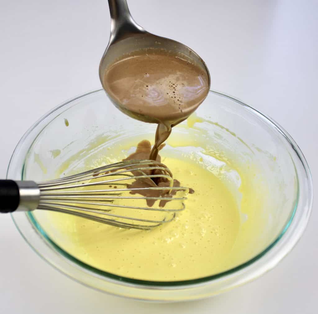 chocolate custard being whisked into egg yolks in glass bowl