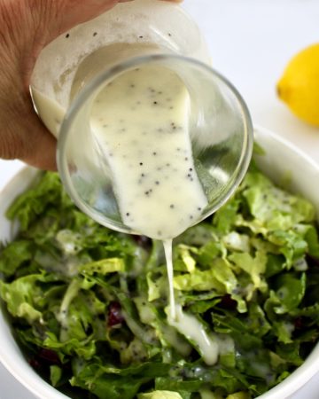 Lemon Poppy Seed Dressing being poured over lettuce in white bowl