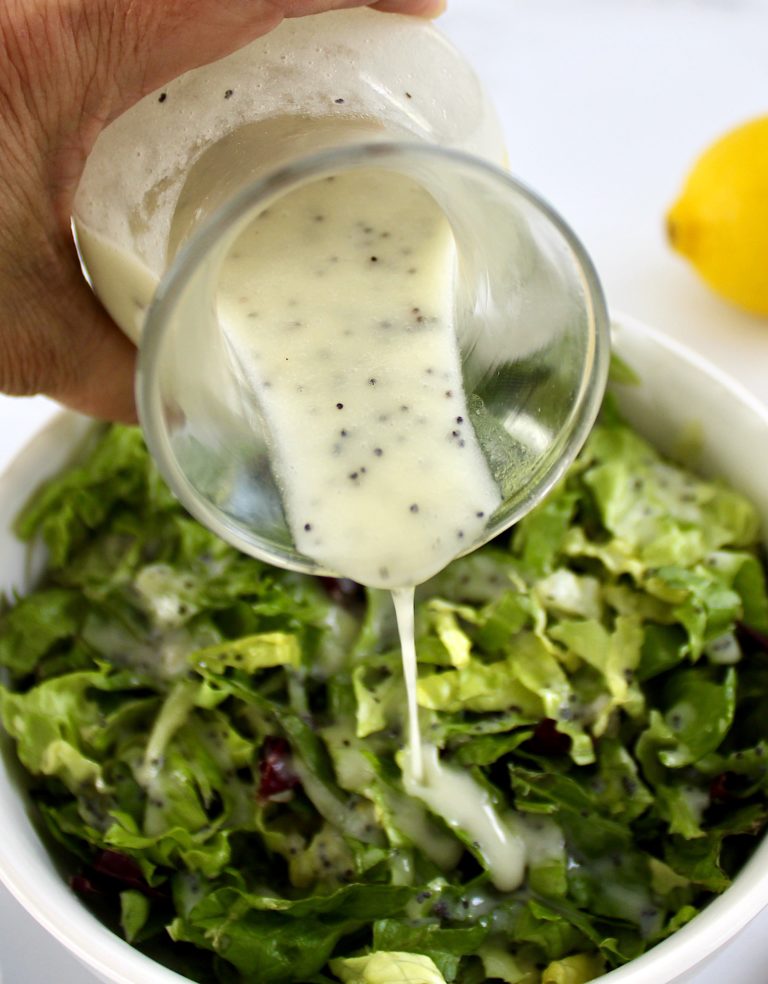 Lemon Poppy Seed Dressing being poured over lettuce in white bowl