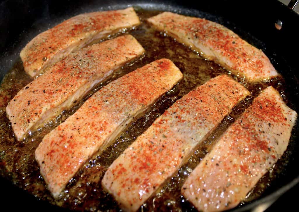 6 seasoned filets of salmon frying in skillet