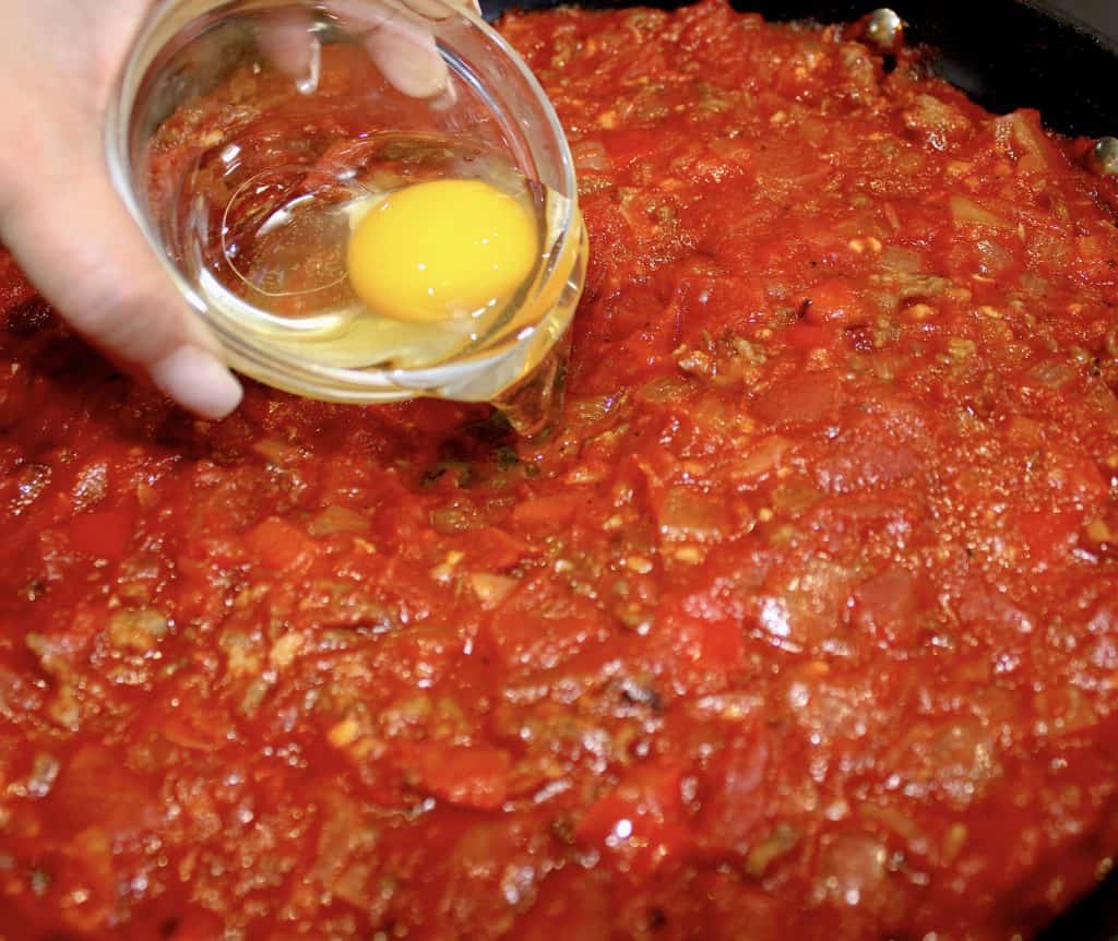 chunky sausage tomato sauce with whole raw egg being poured into sauce