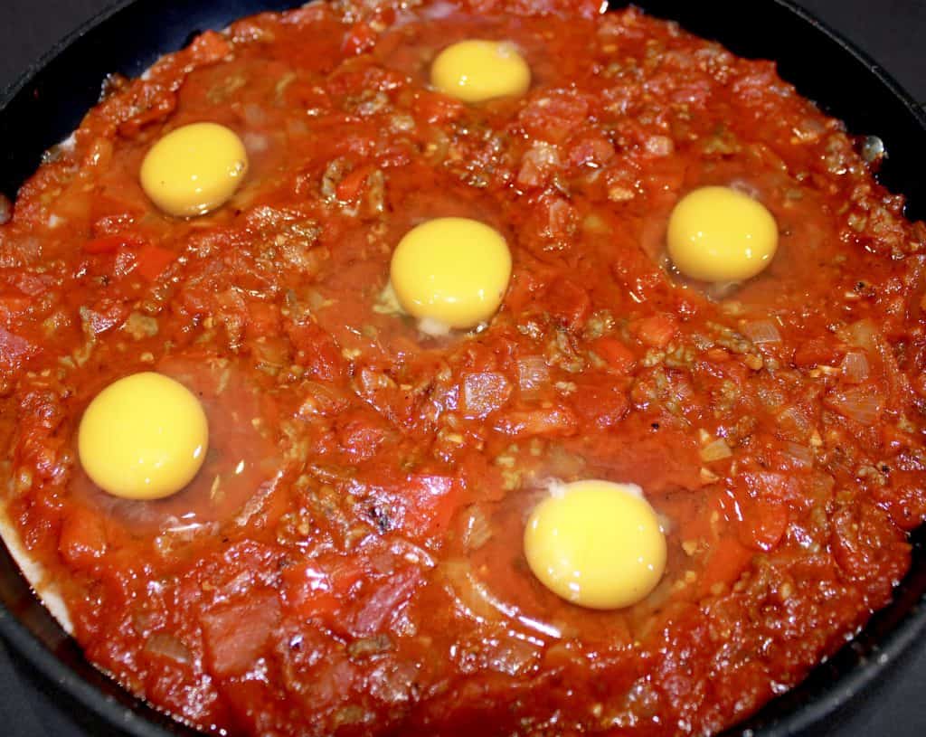 6 raw eggs over shakshuka tomato sauce in skillet