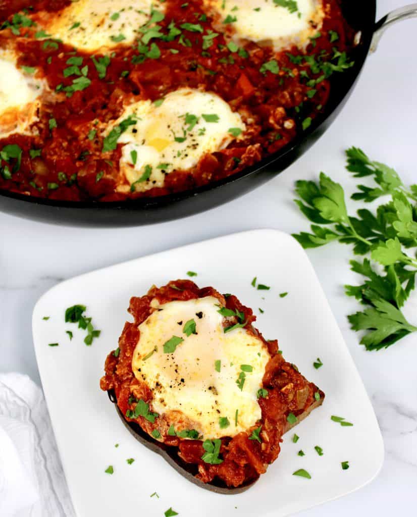 Shakshuka with Italian Sausage over toast on white plate skillet in background