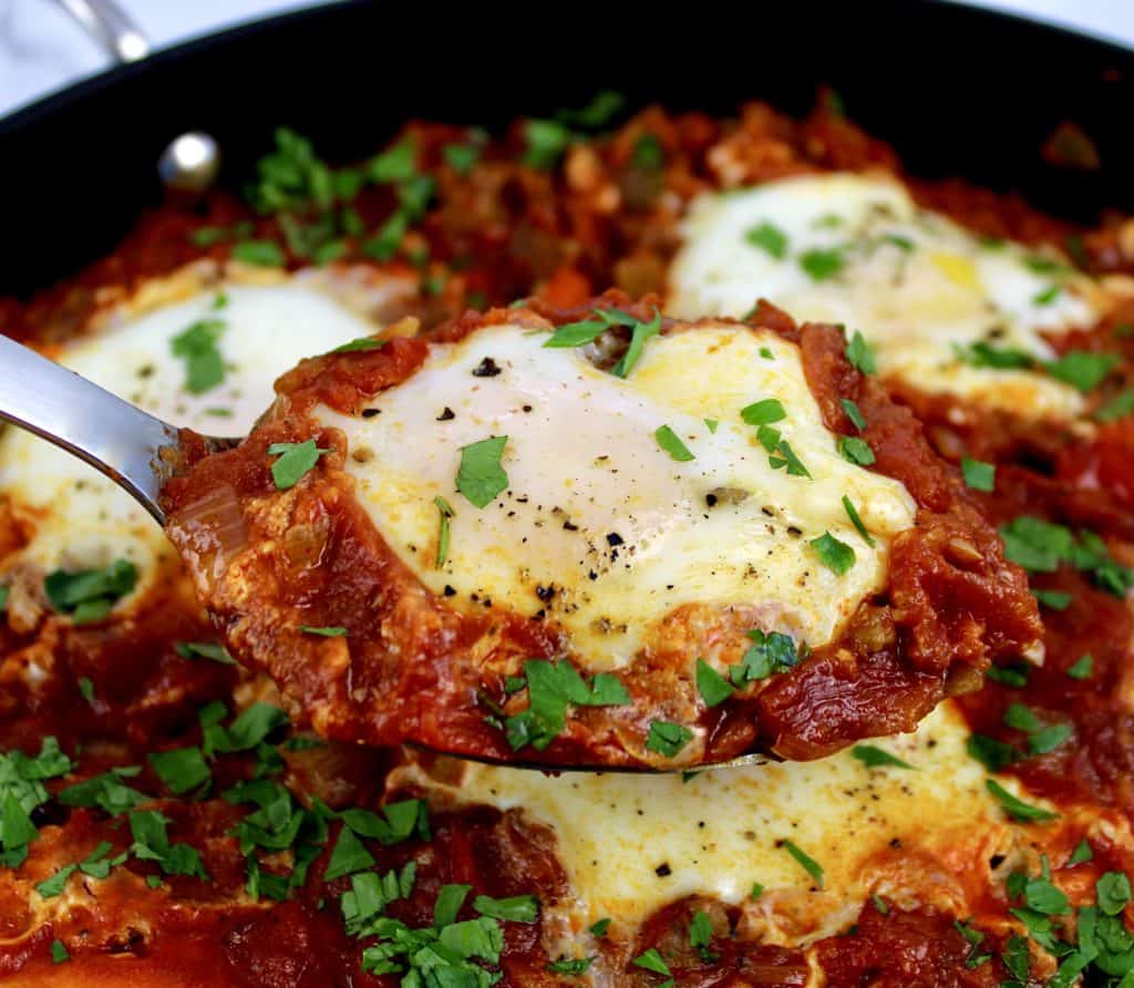 Shakshuka with Italian Sausage with parsley garnish being spooned out of skillet