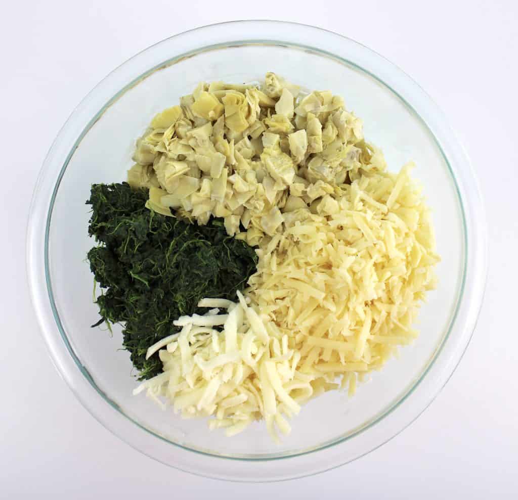 spinach chopped artichokes and white cheeses in glass bowl unmixed